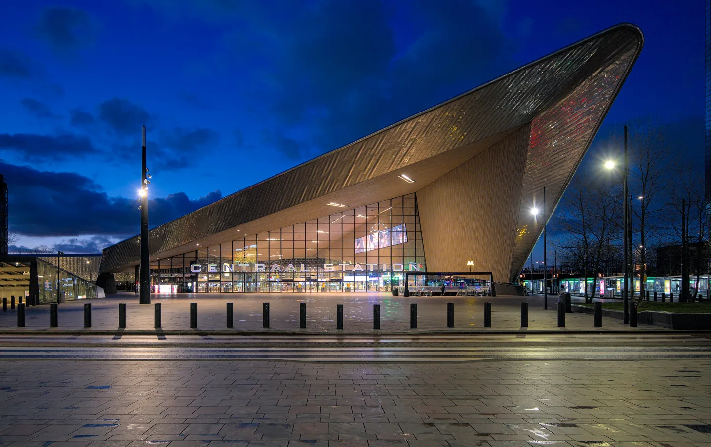 De hoekige stationskap van Rotterdam Centraal met het verlichte stationsplein in de avond