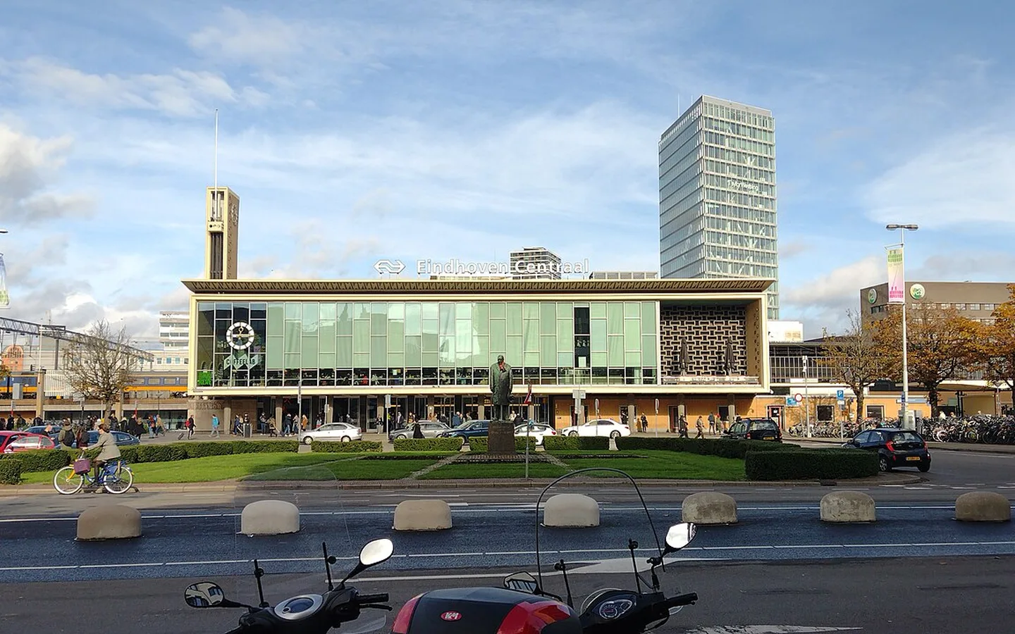 De moderne stationsgevel van Eindhoven Centraal met het klokgebouw, een standbeeld en een glazen kantoortoren op het plein