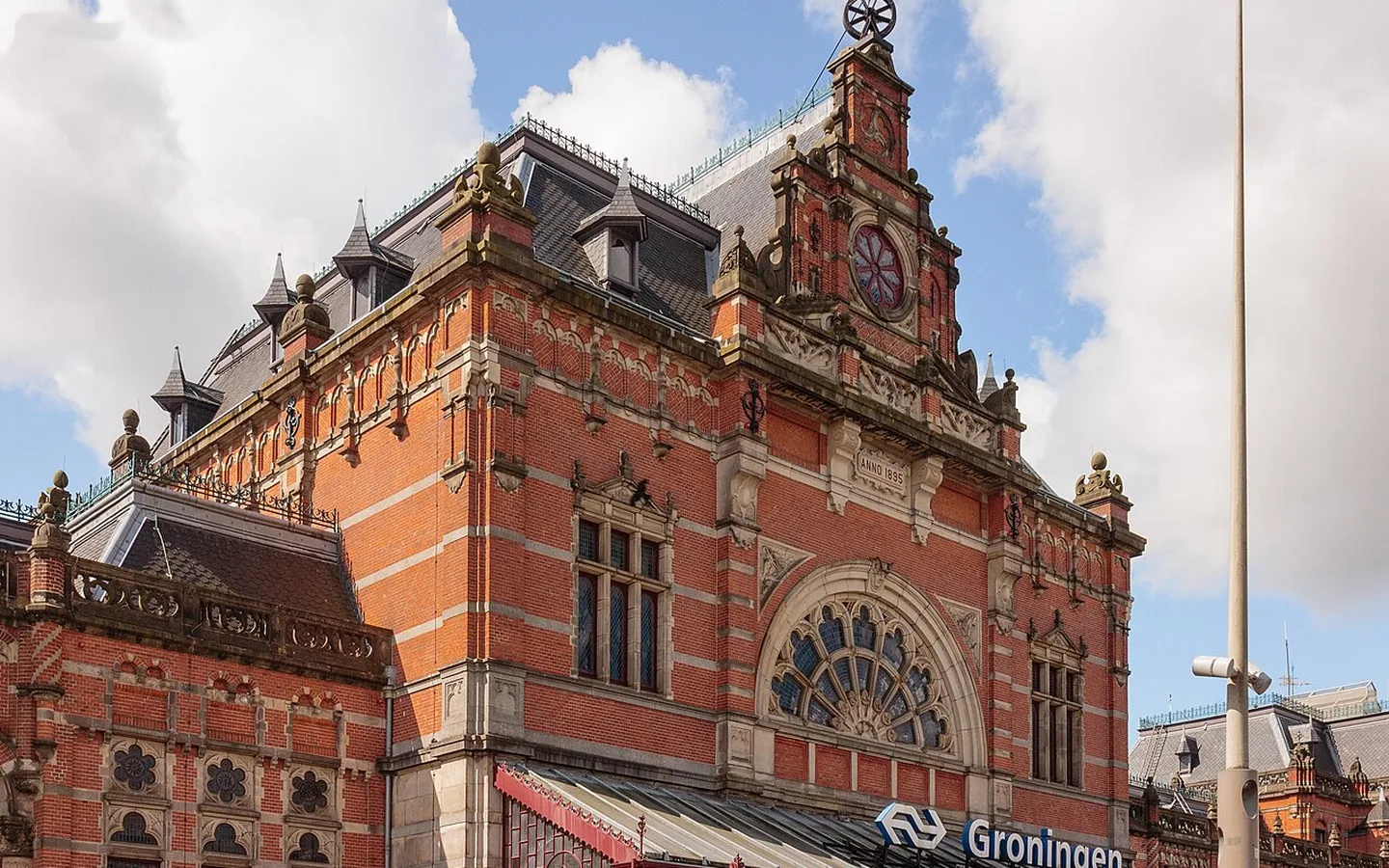 De rijk versierde rode bakstenen voorgevel van station Groningen met klok, rond venster en het naambord