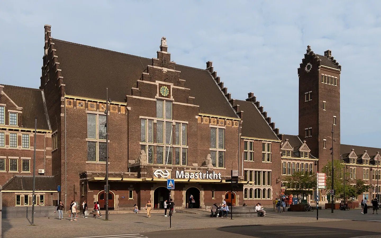 Het historische bakstenen stationsgebouw van Maastricht met klok, hoektoren en het plein op de voorgrond